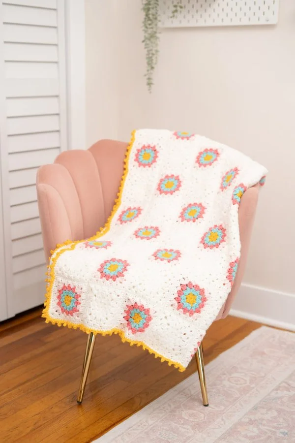 A pastel coloured flower granny square blanket with a yellow border.