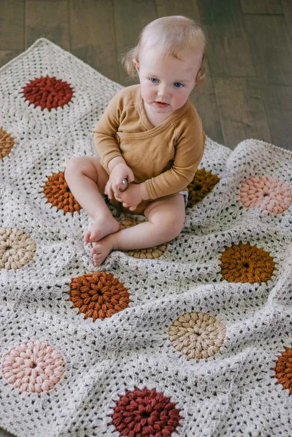 A baby sitting on a granny square blanket.