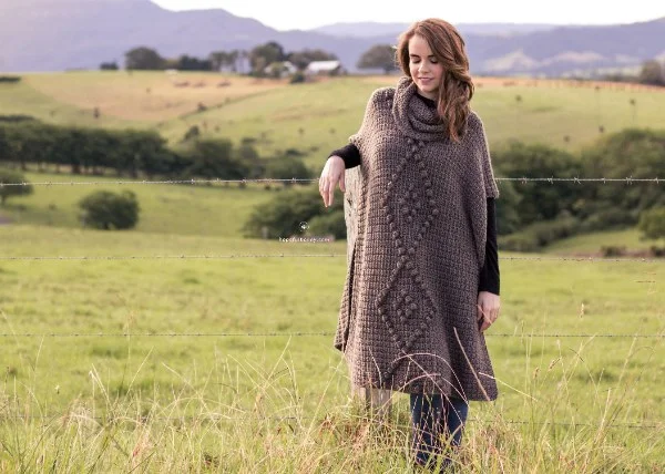 A woman in a filed weraing a long brown crochet poncho.