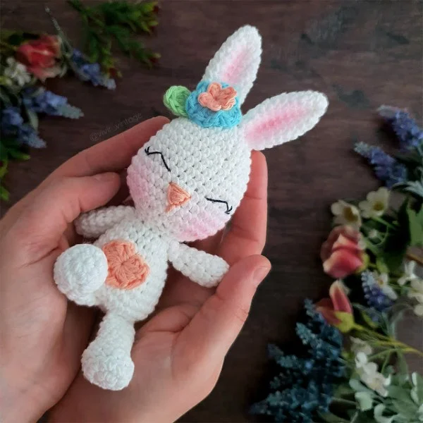 A white toy crochet rabbit laying in the palms of hands.