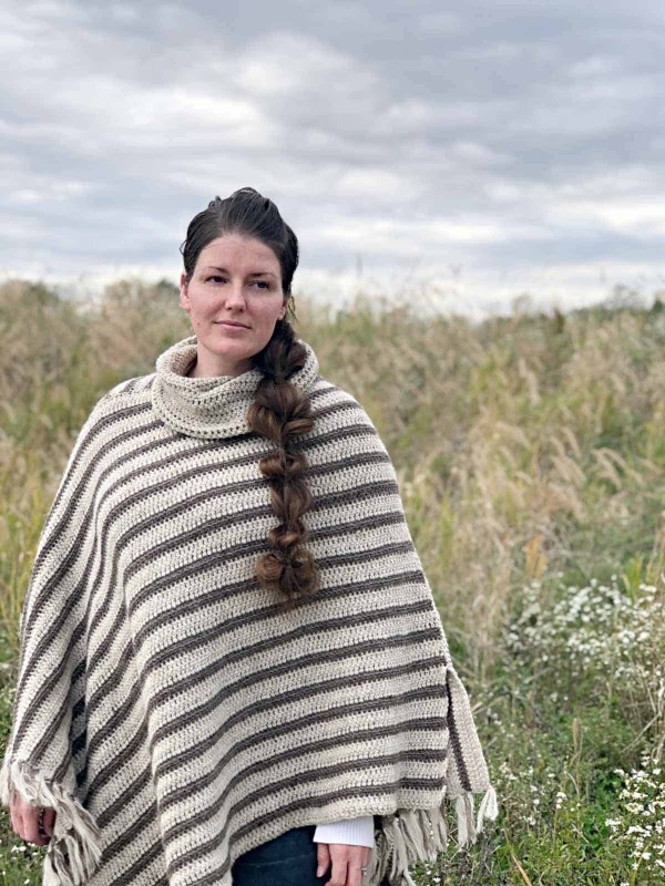 A woman wearing a striped, assymetrical crochet poncho.