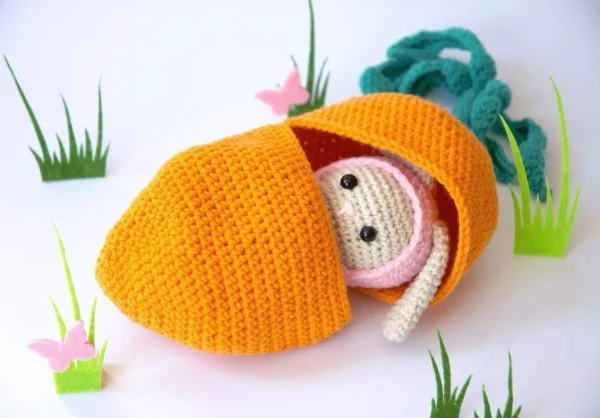 A baby crochet bunny in a carrot-shaped bed.