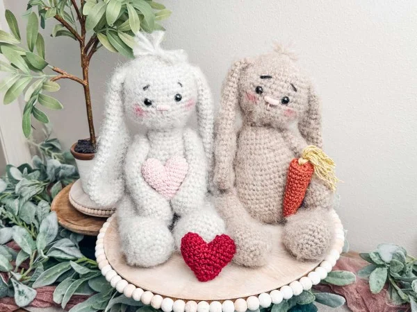 Two floppy crochet bunnies holding valentines hearts.