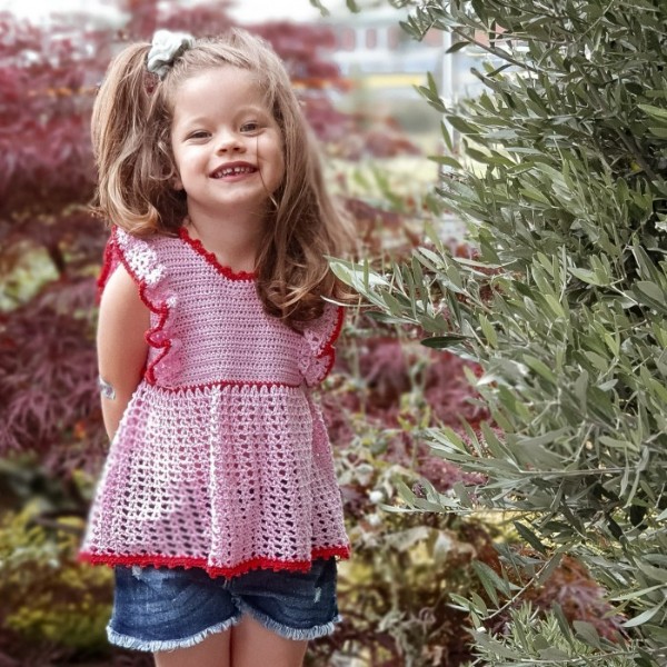 A young girl wearing a pink crochet top with ruffle sleeves.