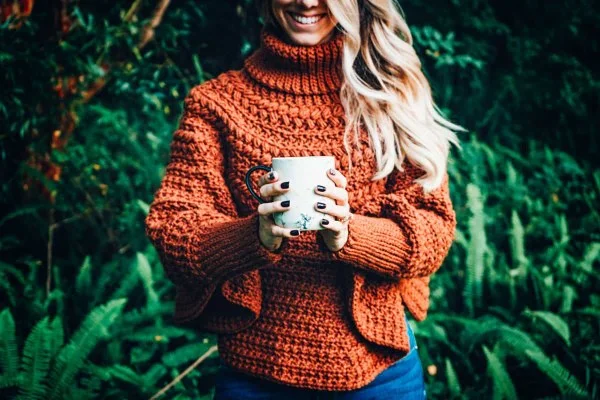 A woman wearing a brick red crochet poncho with ribbed sleeves.