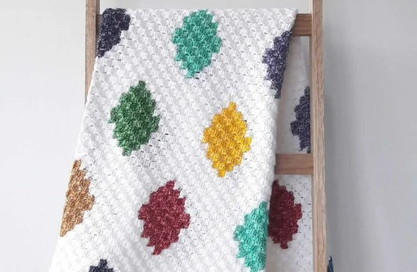 A colourful c2c crochet blanket hanging on a wooden ladder.