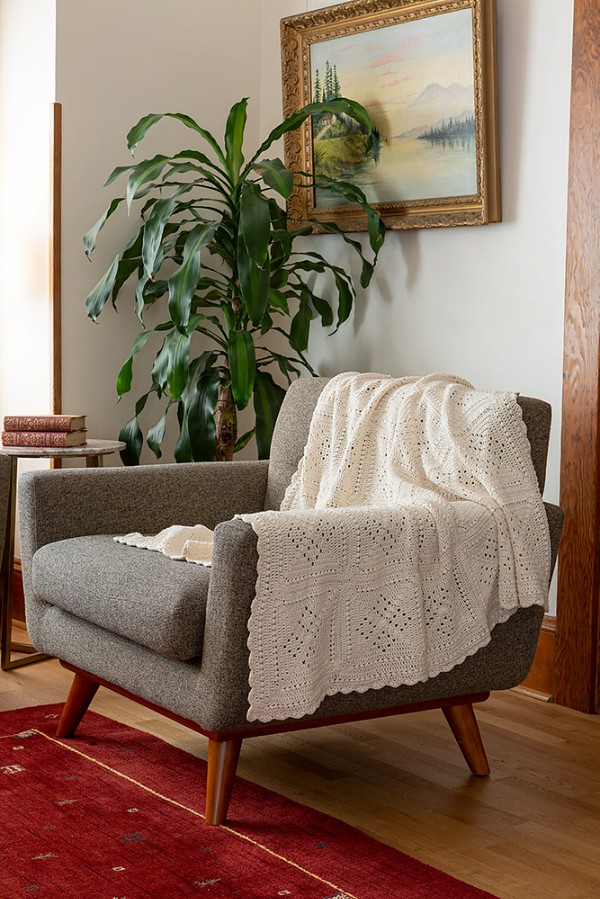 A filet crochet granny square blanket draped over a lounge chair.