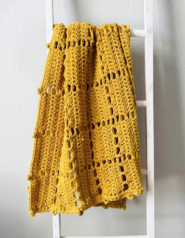 A bright yellow filet crochet blanket with a cute picot edge.