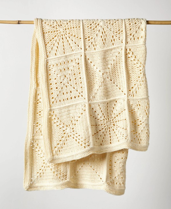 A filet crochet sampler blanket hanging over a wooden rod.