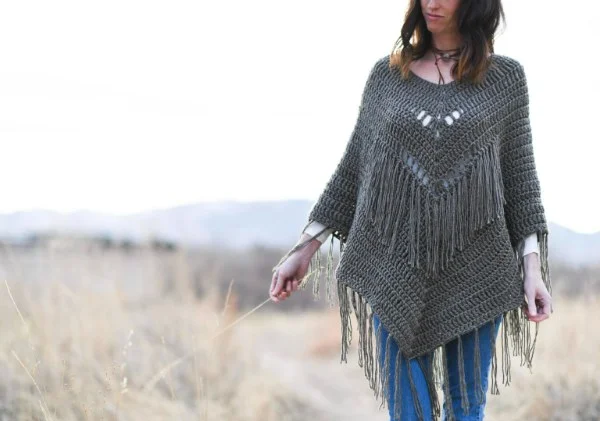 A woman wearing a grey crochet poncho with lots of fringing.