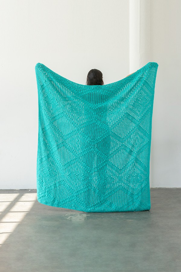 A woman holding up a large filet crochet blanket.