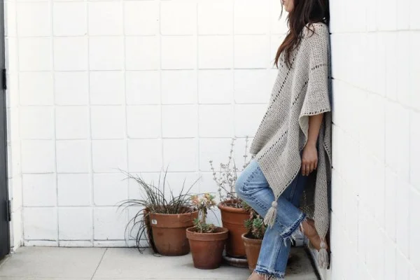 A woman waearing a long crochet poncho with jeans.