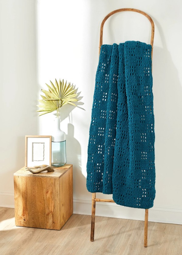 A teal blue filet crochet blanket draped over a timber ladder.