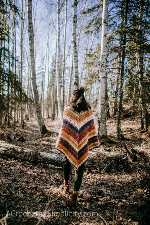 A woman in the woods wearing a classic striped crohet poncho.