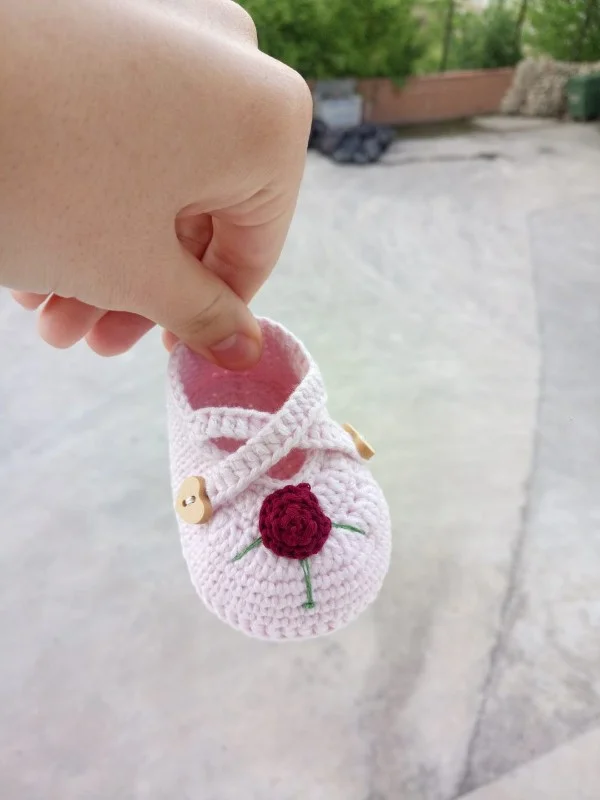 A pale pink crochet Mary Jane baby shoe with flower applique.