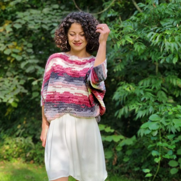 A womna wearing a brightly coloured, cropped length batwing crochet sweater.