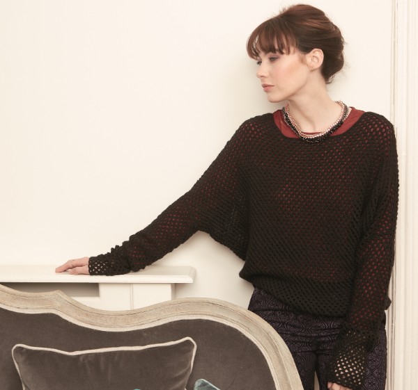 A woman wearring a black batwing crochet sweater with an open mesh stitch.