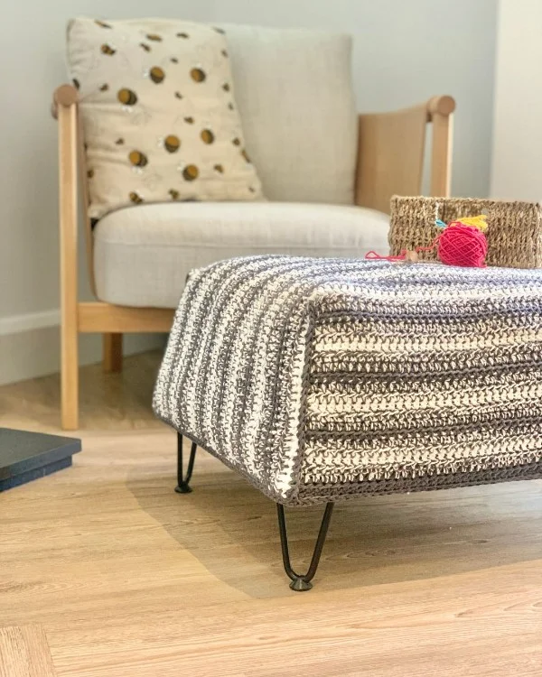 A grey and white striped crochet footstool with hairpin legs.