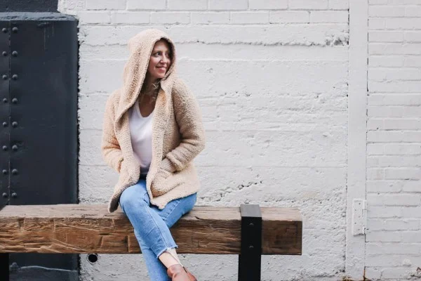 A woman sitting on a bench, wearing a crochet hoodie with pockets.