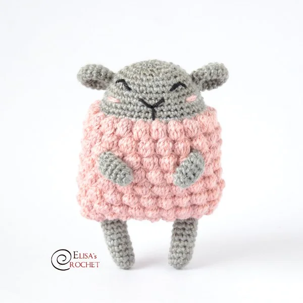 A grey crochet sheep with a pink bobble stitch fleece.