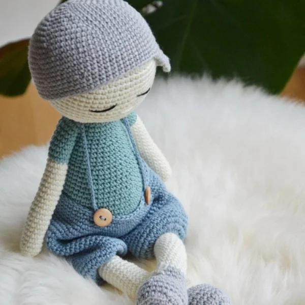 A crochet boy doll with overalls and a cap.