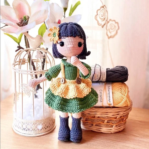 A detailed crochet doll with a green dress and a yellow apron.