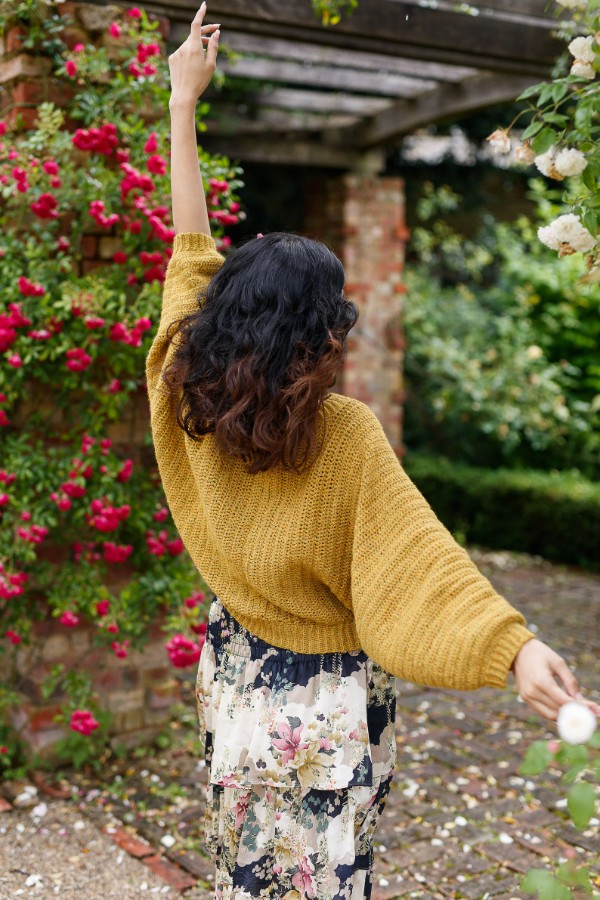 A woman wearing a mustard yellow batwing crochet pullover.