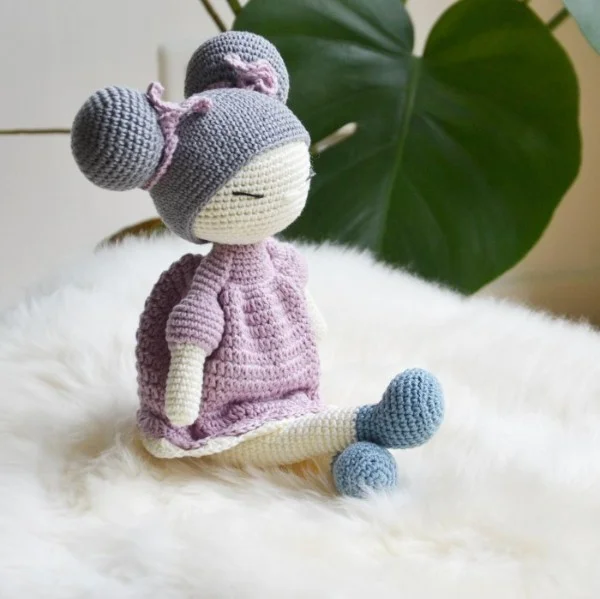 A crochet dol with a pink dress and bun hair style.