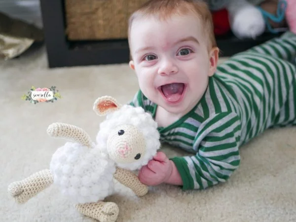 A baby playing with a crochet lamb toy.