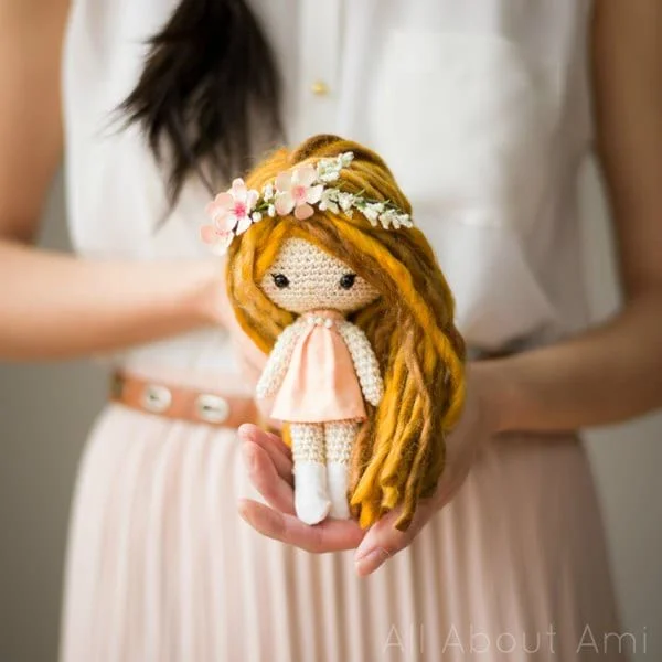 A woman holding a crocheted doll with long yellow hair.