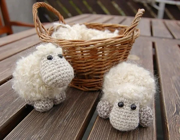 Two small crochet sheep next to a basket of wool.