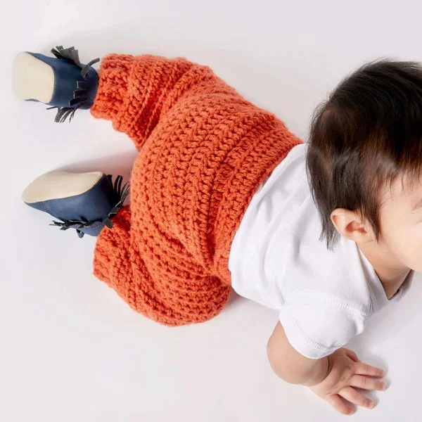 A crawling baby wearing bright orange crochet pants.