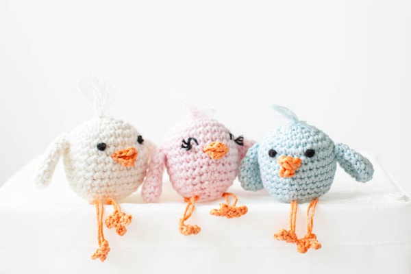 Three pastel-coloured crochet chicks with long legs.