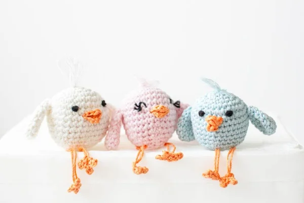 Three pastel-coloured crochet chicks with long legs.