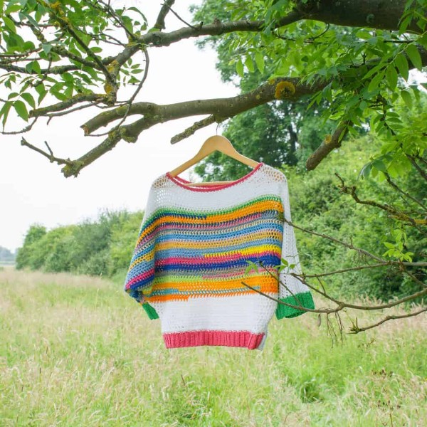 A scrap yarn crochet dolman sleeve sweater hanging in a tree.