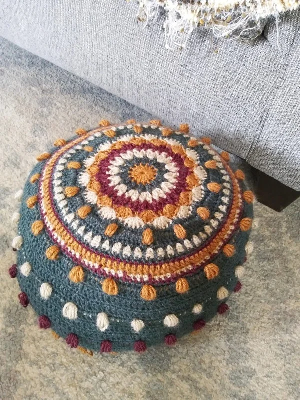 A multi-coloured round crochet pouf with textured stitches.