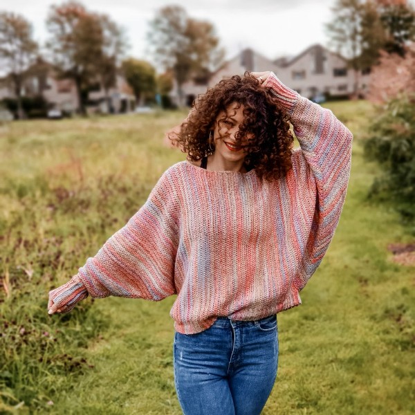 A woman wearing an oversized batwing crochet sweater in pink tones.