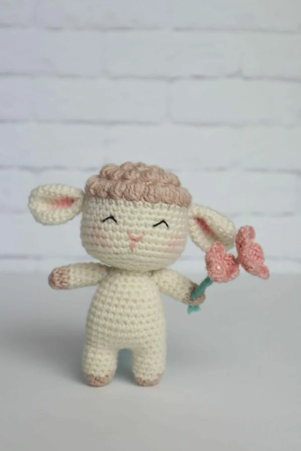 A standing crochet sheep with a bunch of crochet flowers.