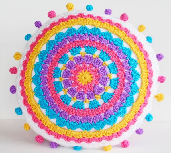 A colourful round crochet cushion with pompom edging.