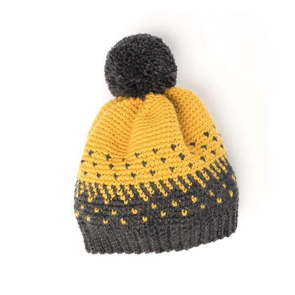 A charcoal grey and yellow colourwork hat with a pompom.