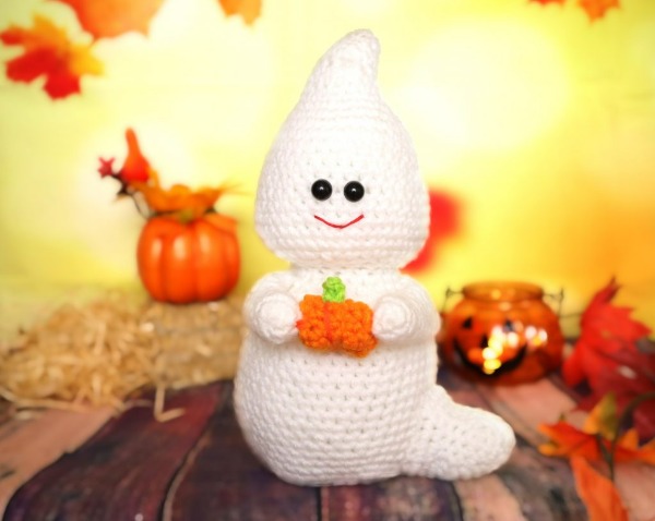 A crochet ghost holding a tiny crochet pumpkin.