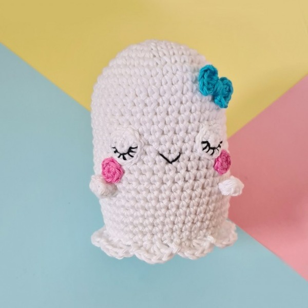 A crochet ghost with rosy cheeks and a blue hair bow.