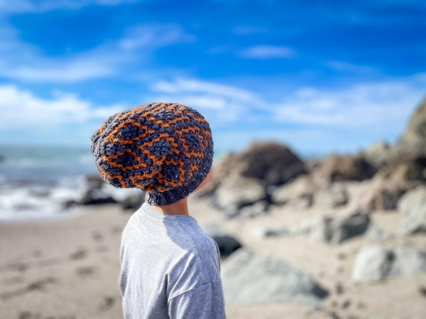 A child at the beach wearing a colourwork crochet beanie.