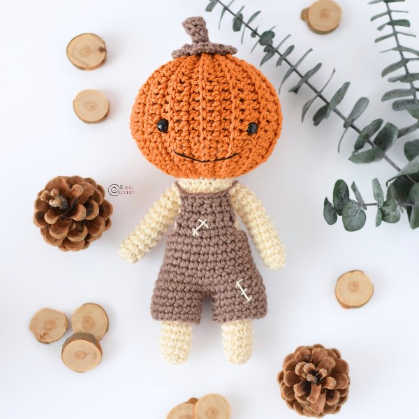 An amigurumi crochet doll with a pumpkin head.