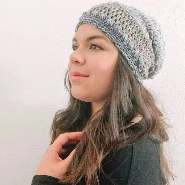 A woman weairng a crochet slouchy beanie in grey tones.