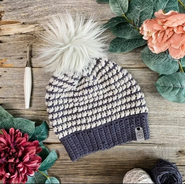 A black and white crochet slouchy beanie with a faux fur pompom.