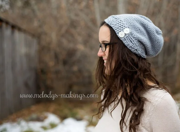 A woman aearing a light grey crochet slouchy beanie with a buttoned brim.