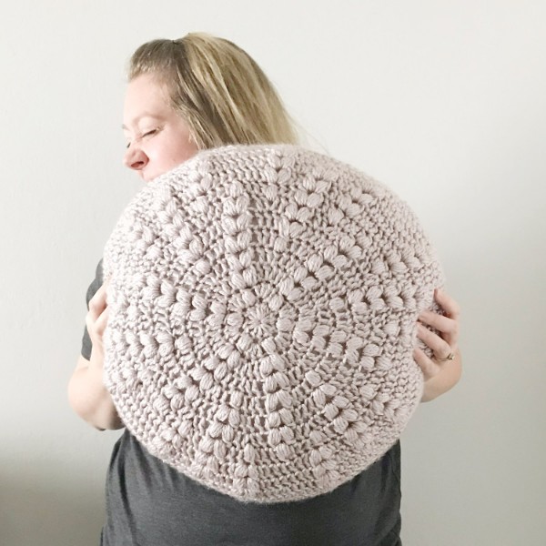 A woman holding a round, textured crochet pillow.