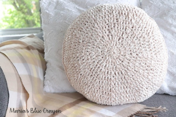 A cream coloured circle pillow crocheted in velvet-style yarn.