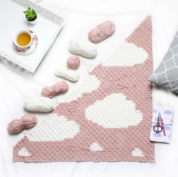 A pink c2c baby blanket with cloud motifs.